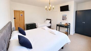 A hotel room with a large bed, a bedside table, a wardrobe, a television on the wall, and a chandelier.