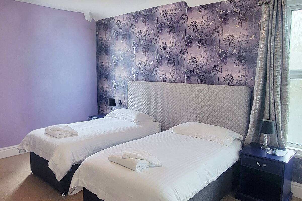 A hotel room with two beds, a nightstand, and a window with curtains.