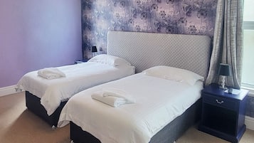 Een hotelkamer met twee bedden, een nachtkastje en een raam met gordijnen.