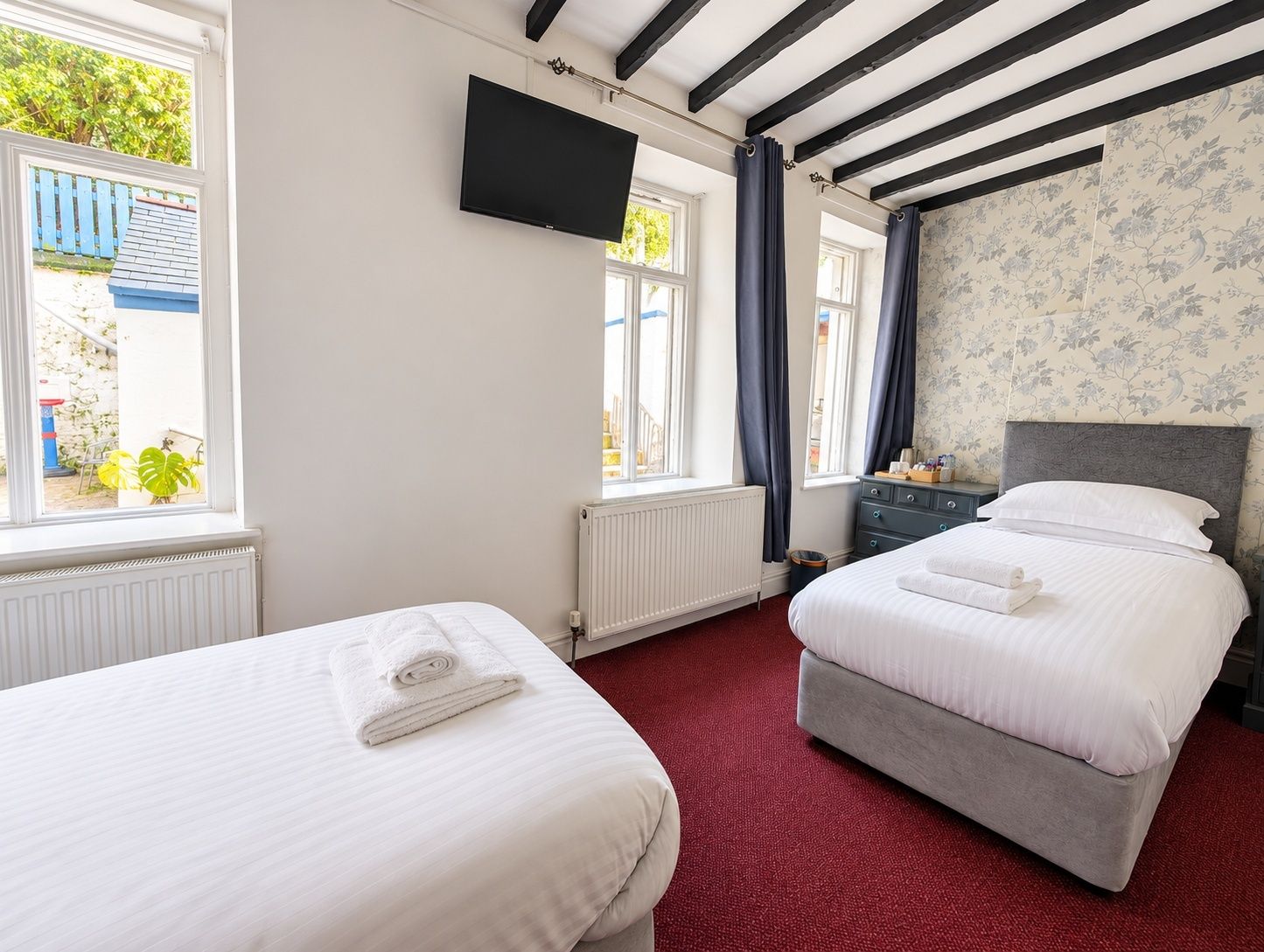 A hotel room with two beds, a TV mounted on the wall, and a view of the outside.