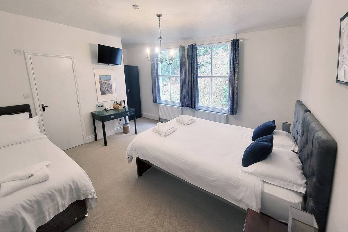 A hotel room with two beds, a desk, a TV, and a window with curtains.