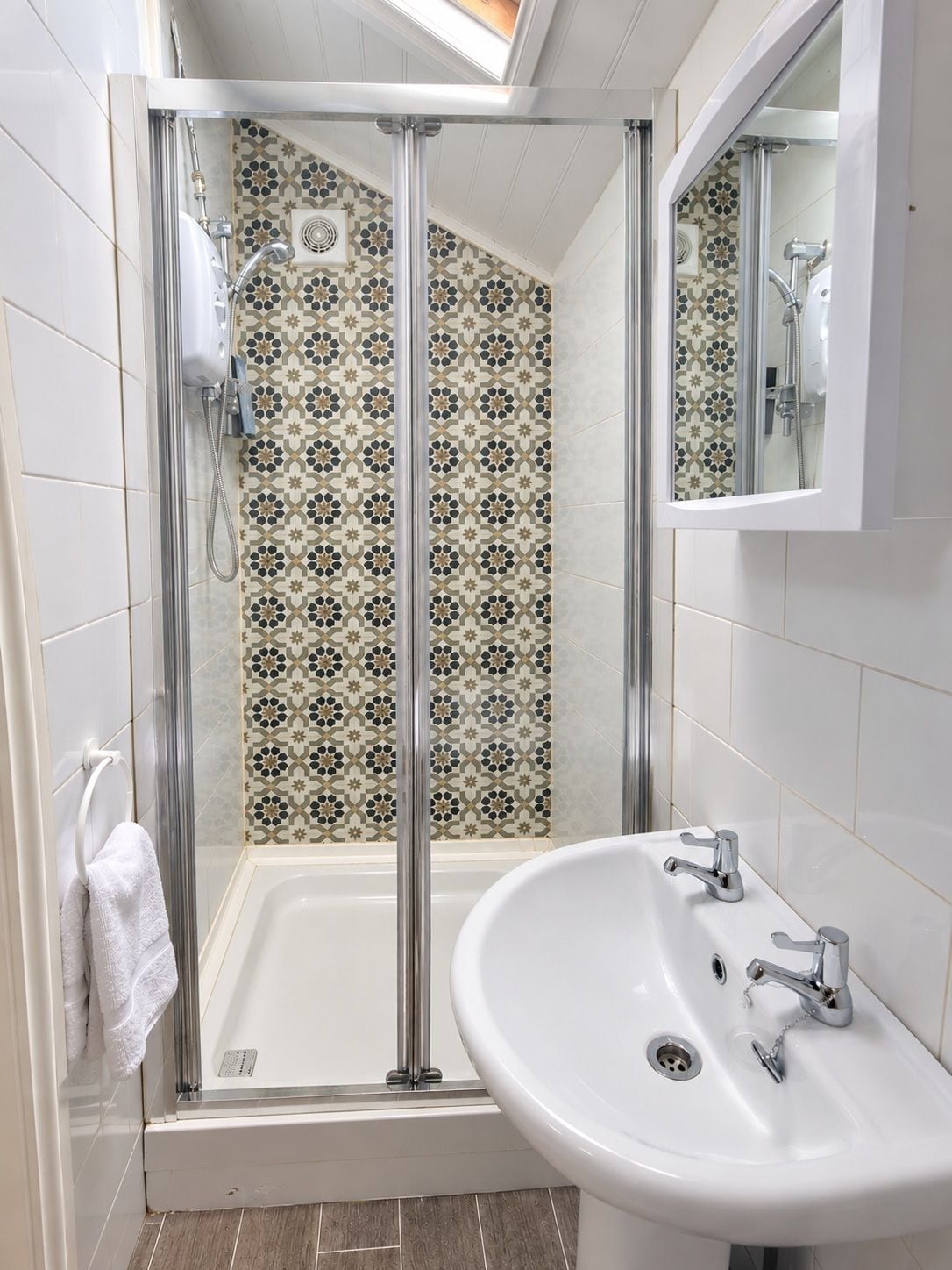 A modern bathroom with a glass-enclosed shower, a white sink, and patterned tiles.