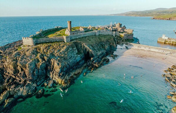 A coastal fortification with a rugged cliffside and a beach in the foreground. - Kings' House (Douglas)