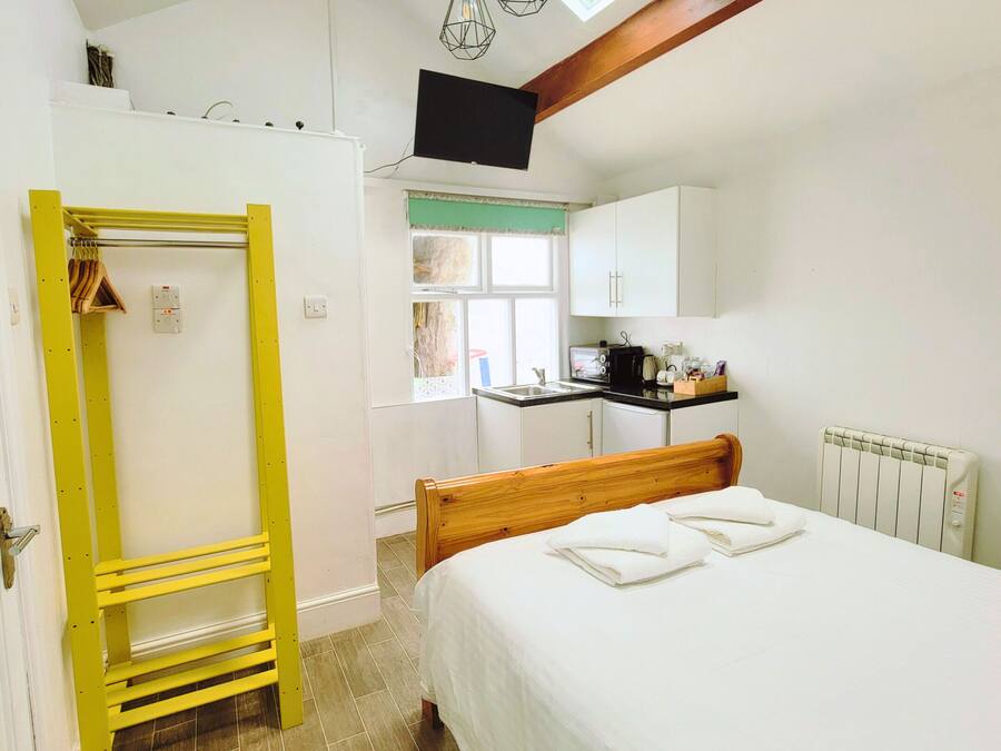 A bedroom with a bed, a yellow shelf unit, a window with a view, and a kitchen area.