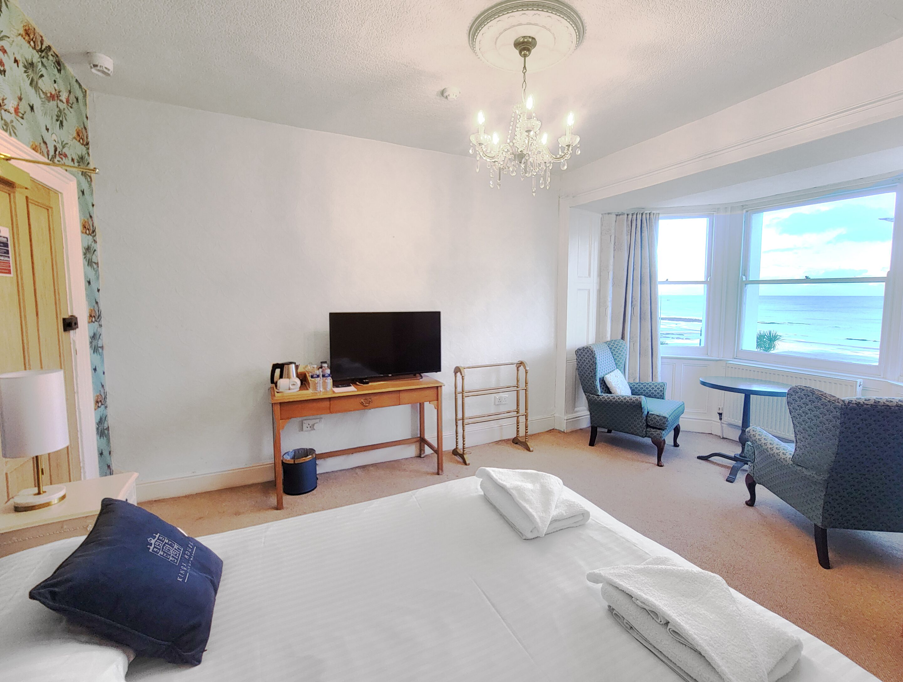 Habitación de hotel con cama, escritorio con televisor, silla, mesa y vista al mar.