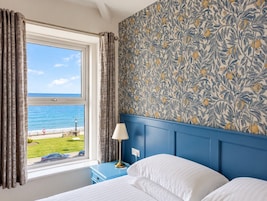 Habitación de hotel con cama, mesita de noche con lámpara, ventana con cortinas y pared con estampado floral.