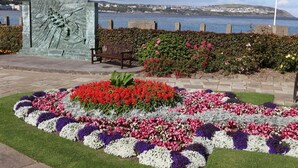 A landscaped garden with a bench, flowers, and a sculpture. - Kings' House (Douglas)