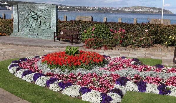 A landscaped garden with a bench, flowers, and a sculpture. - Kings' House (Douglas)