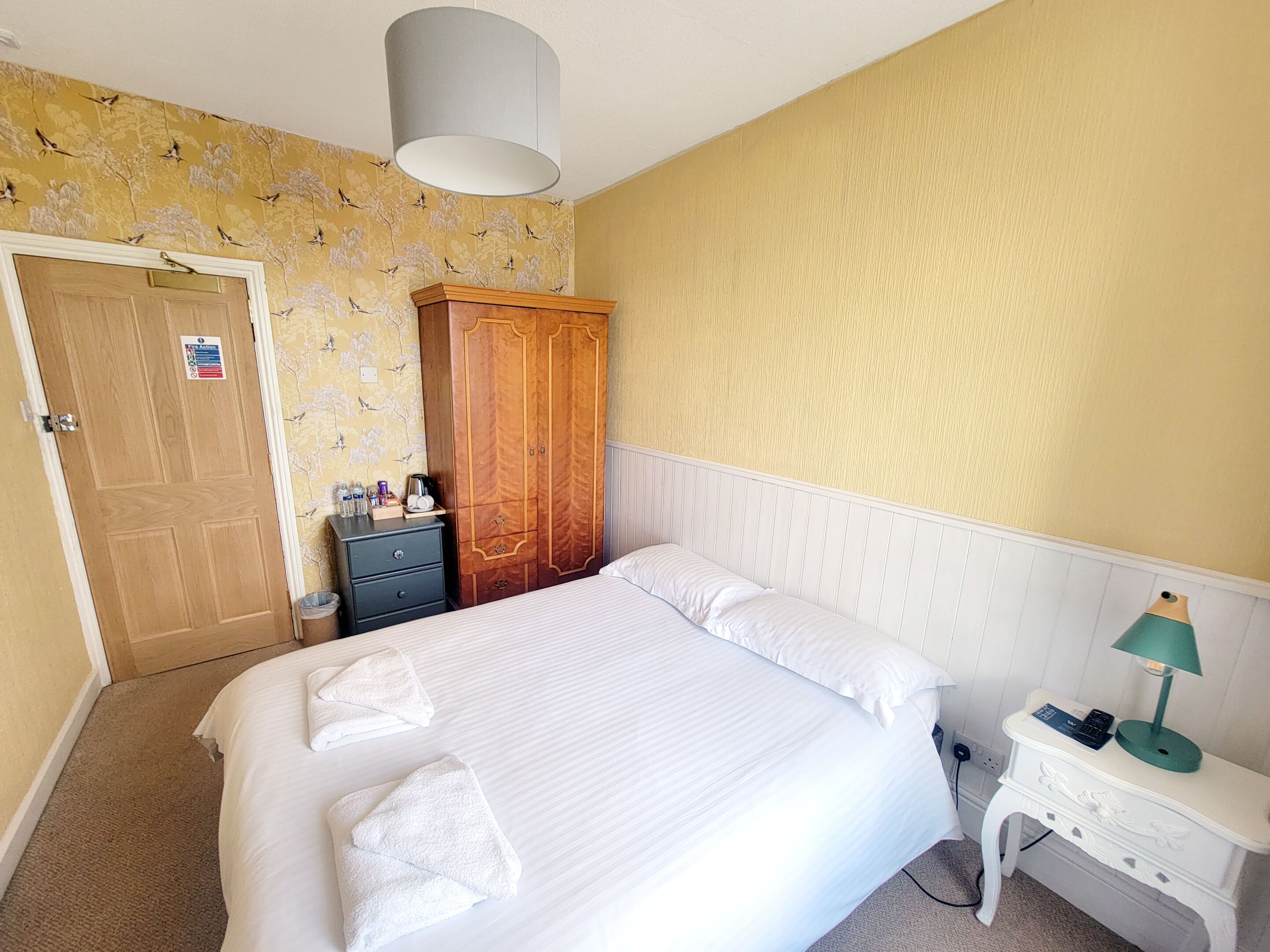 A hotel room with a bed, a nightstand, a wardrobe, and a door with a sign.