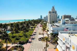 Un paysage urbain côtier avec une plage, une promenade bordée de palmiers et des bâtiments modernes.