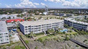 Un hotel de varios pisos con piscina en la azotea, rodeado de vegetación y un puente al fondo.