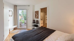 Un dormitorio con cama, una banca, una puerta que da a un balcón y una estantería con adornos.
