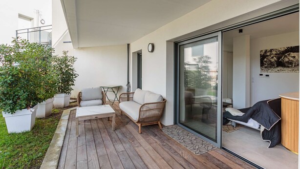 Un patio moderno al aire libre con piso de madera, un sofá blanco, una mesita y macetas con plantas.