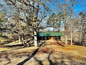 A rustic cabin with a green roof, surrounded by trees and a dirt path leading to it. - Buffalo Cabin Gorgeous Illinois River view (Tahlequah)