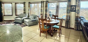 Un salon comprenant un canapé, des fauteuils, une table à manger et offrant une vue dégagée grâce à de grandes fenêtres.
