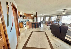 A spacious living area with a large sofa, a kitchen with wooden cabinets, and a dining area with bar stools. - Buffalo Cabin Gorgeous Illinois River view (Tahlequah)