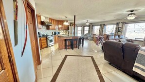 A spacious living area with a large brown sofa, a kitchen with wooden cabinets, and a dining area with bar stools. - Buffalo Cabin Gorgeous Illinois River view (Tahlequah)
