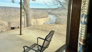 A covered patio with a metal chair, a view of a river, and a tree. - Buffalo Cabin Gorgeous Illinois River view (Tahlequah)