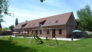 Ein Backsteinhaus mit geneigtem Dach, einer Schaukel und einer Terrasse mit Sitzgelegenheiten.
