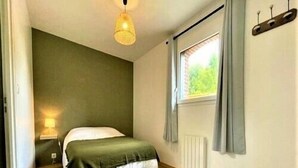 Ein Schlafzimmer mit Bett, einem Fenster mit Vorhängen, einem Heizkörper und einer Wandleuchte.