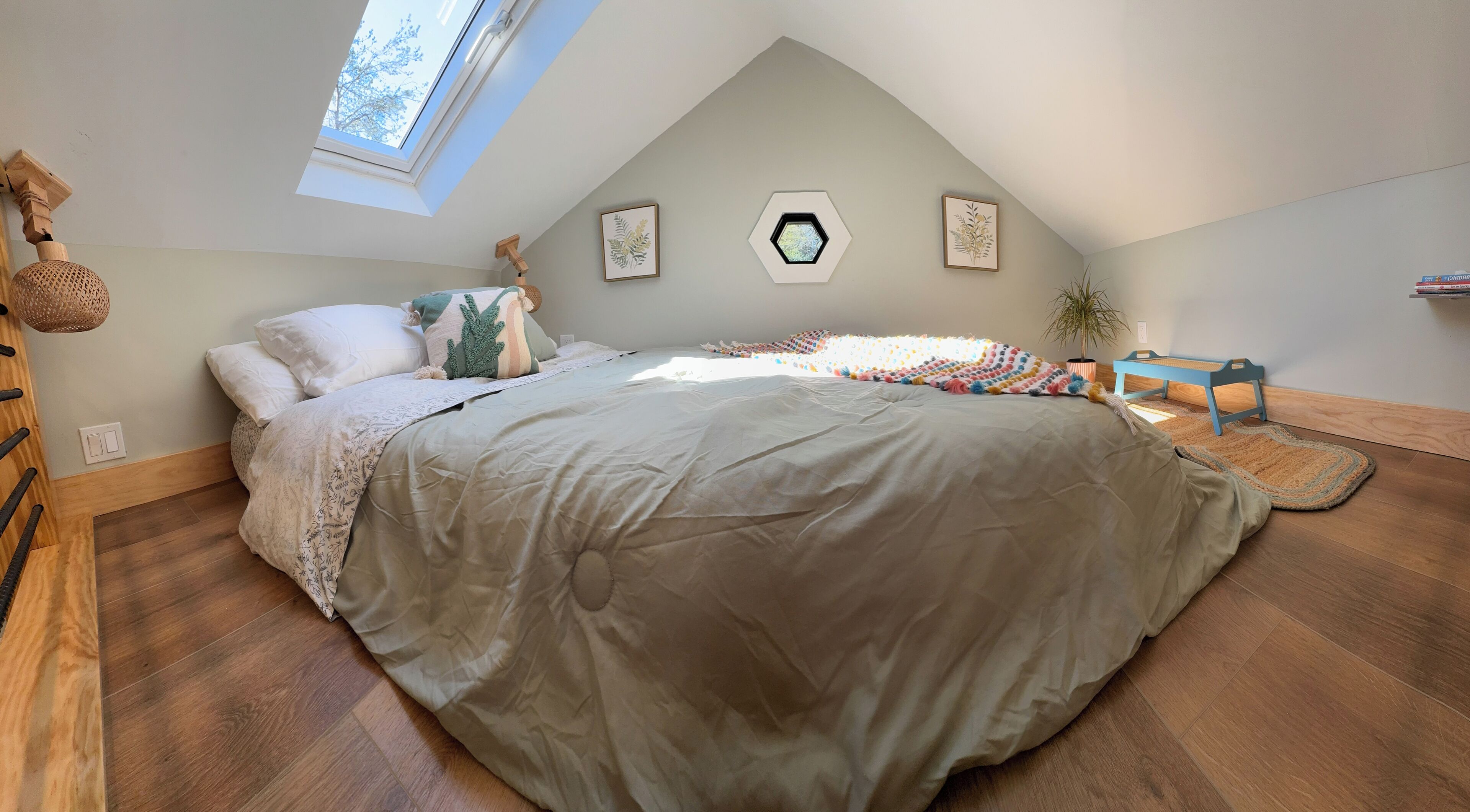 A bedroom with a large bed, a skylight, a wooden dresser, and a small table.