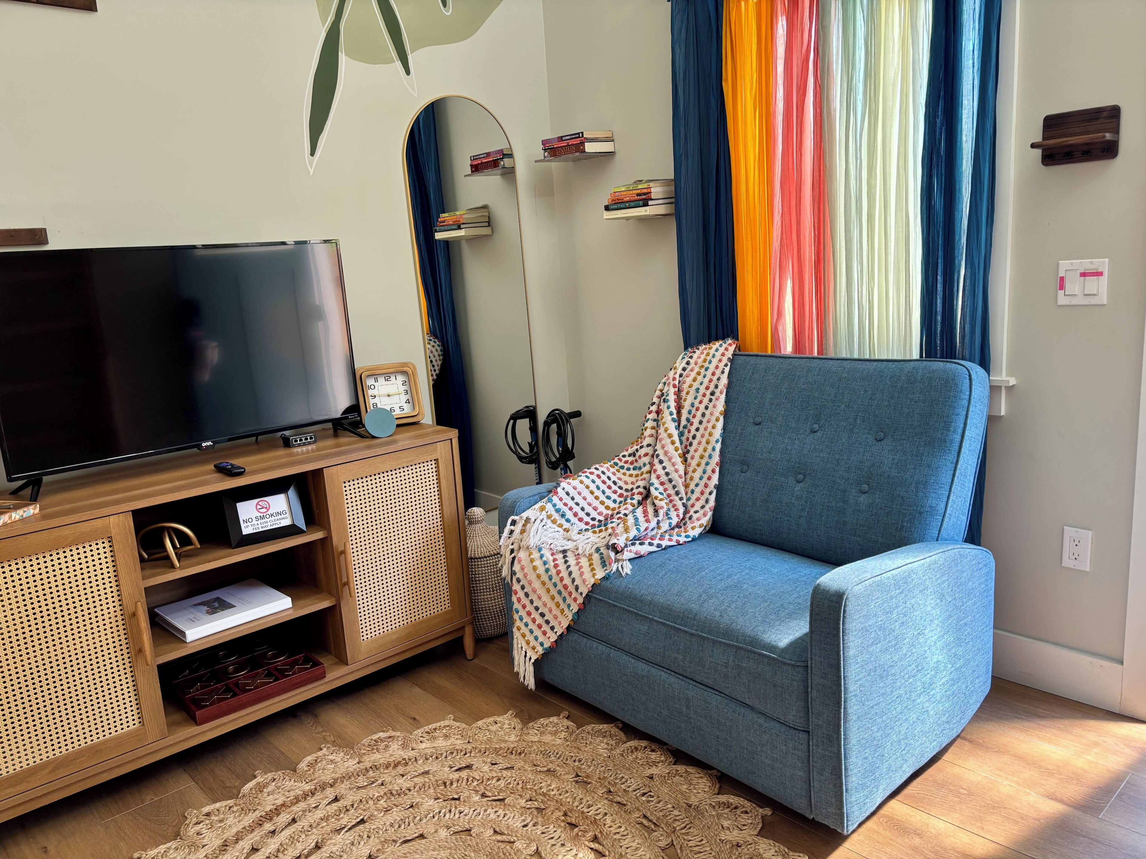 A living room with a TV, wooden entertainment unit, blue sofa, and a woven rug.