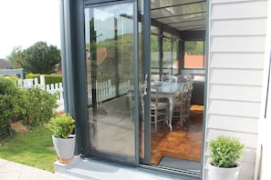 A covered patio with a table and chairs, a white fence, and potted plants.