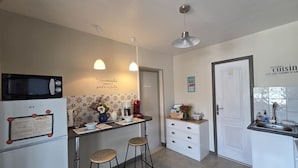 Cocina compacta con microondas, cafetera y una pequeña isla con taburetes.