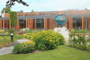 A modern building with a glass facade, a large globe sculpture, and a well-maintained garden with various plants.
