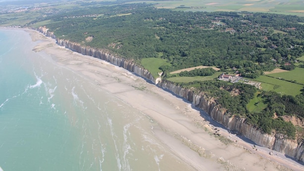Vista aérea de una zona costera con playa, acantilados y un pueblo pequeño.