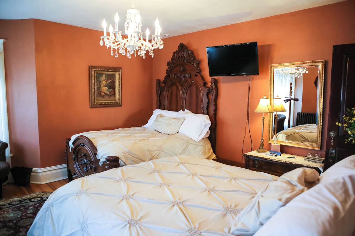 A bedroom with two beds, a chandelier, a television, and a mirror.