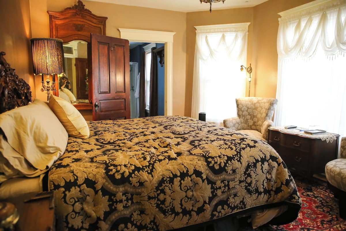 A bedroom with a large bed, a wooden wardrobe, a chair, and a nightstand.