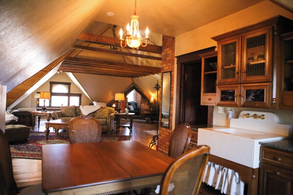 A cozy attic room with a dining table, chairs, a chandelier, and wooden cabinets. - B&B on Broadway (Decorah)