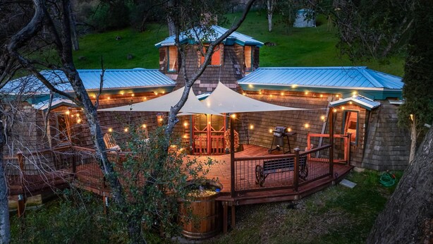 A rustic cabin with a wooden deck, a covered outdoor seating area, and a stone chimney. - Halfling House w/hot tub/firepit/more! (Coarsegold)