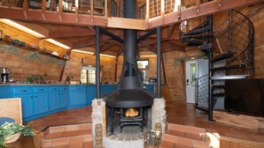 A rustic cabin interior with a stone fireplace, wooden beams, and a blue kitchen. - Halfling House w/hot tub/firepit/more! (Coarsegold)