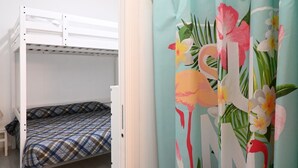 Een stapelbed met een geruit sprei, een klein krukje en een gordijn met een tropisch dessin.