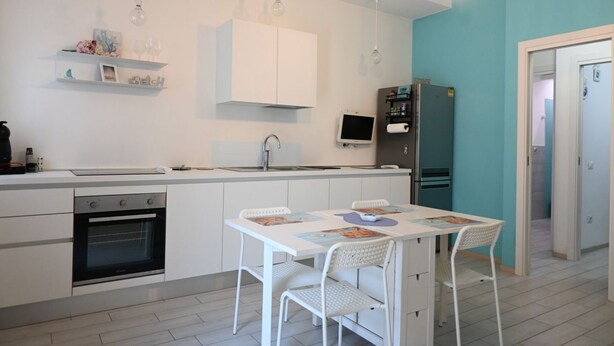 Een moderne keuken met witte kasten, een ingebouwde oven, een eettafel met stoelen en een accentmuur in teal.