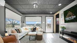 A modern living room with a fireplace, a sofa, a coffee table, and a television displaying 'Copper Top Ridge New Buffalo, Michigan'. - Secluded Retreat, Hot Tub, Fire Pit, Wildlife Views, Near New Buffalo Beach! (New Buffalo)