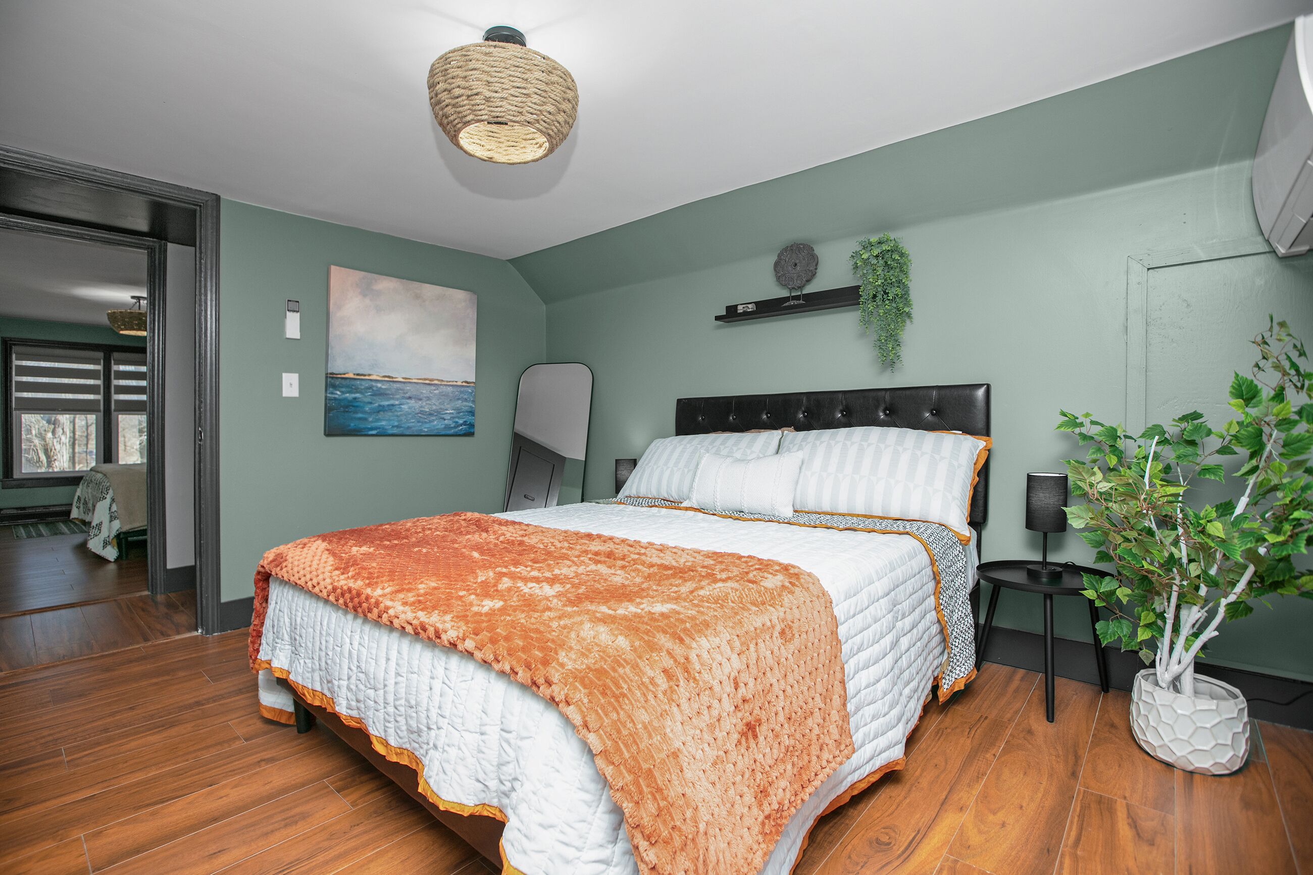 Quarto com uma cama grande, luminária pendente, pintura e planta em vaso.