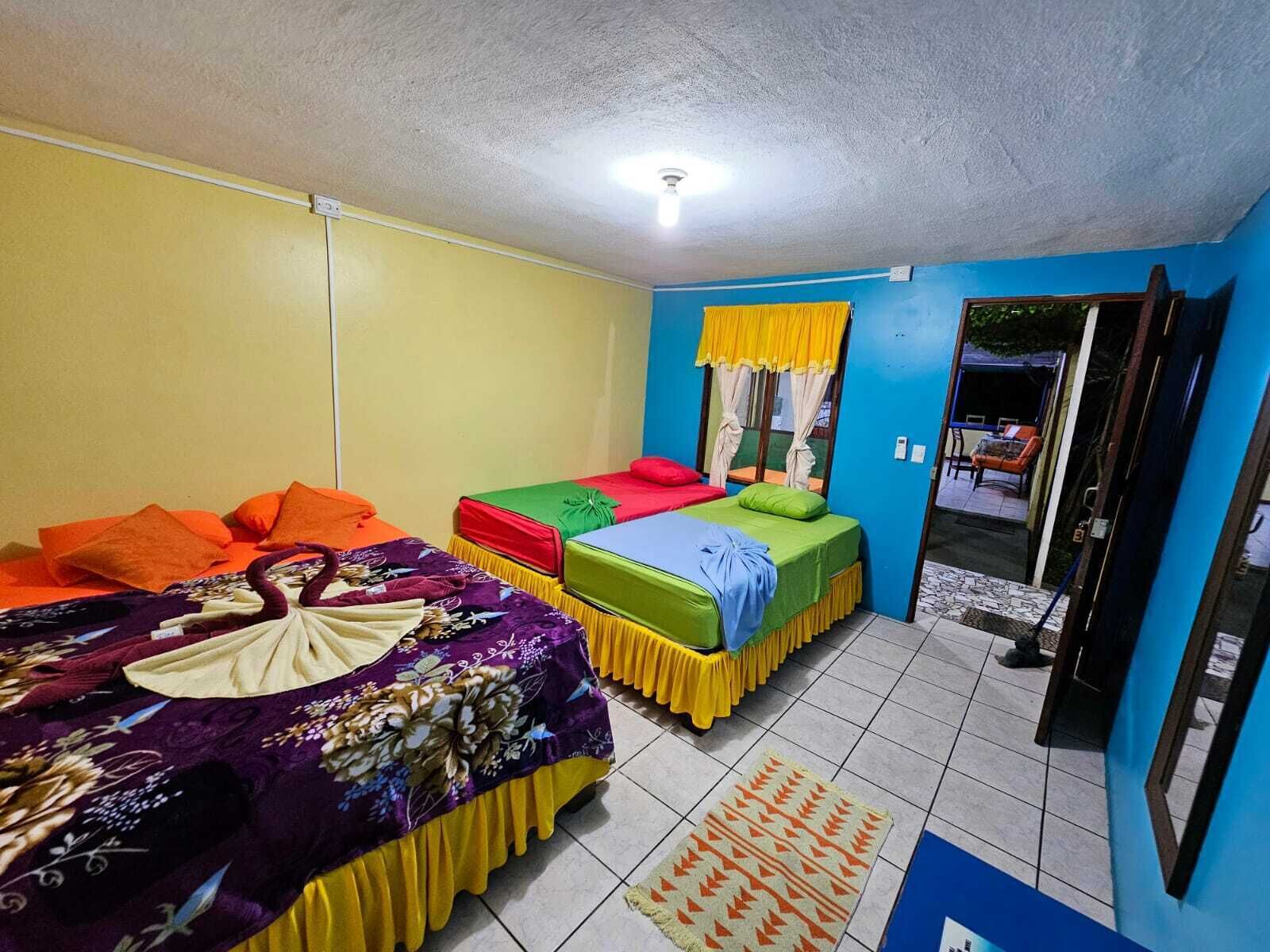 A room with two beds, a window with yellow curtains, and a tiled floor.