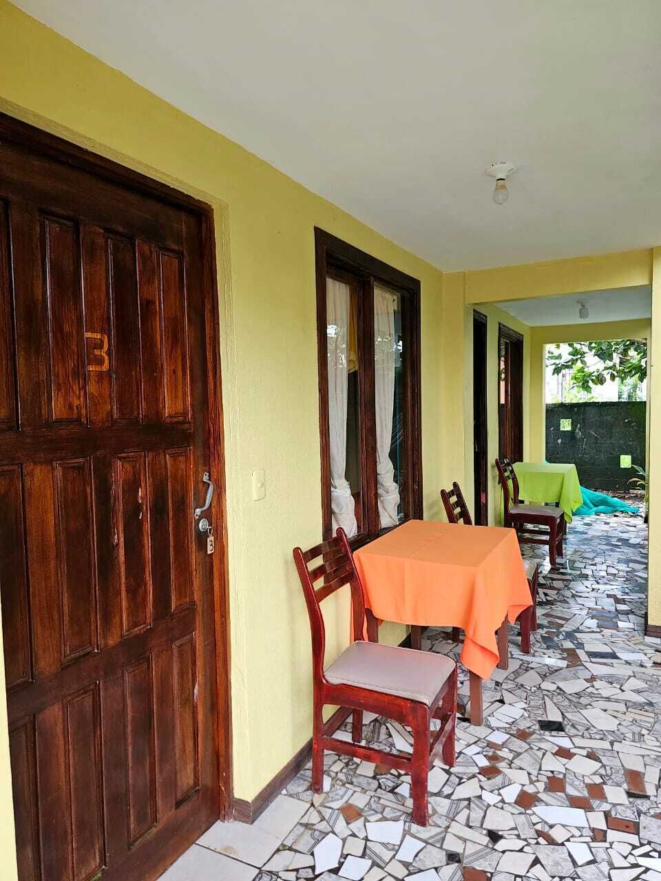 Un pasillo con puerta de madera, suelo de baldosas y una mesa con sillas.