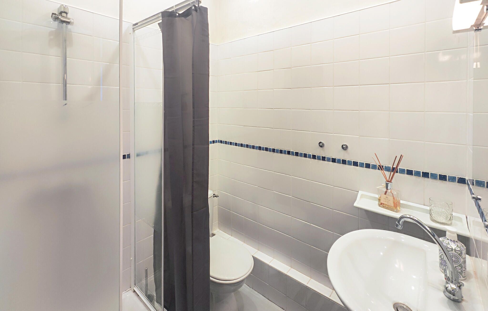 Une salle de bain avec une douche à parois de verre, des toilettes, un lavabo avec un miroir et une bouteille décorative posée sur le lavabo.