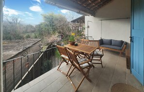 Ein Balkon mit Holztisch und -stühlen, einer Couch und einem Blumentopf.