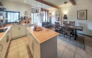 Une cuisine moderne avec des meubles blancs, un grand îlot central et un coin repas comprenant des chaises et une table en bois.