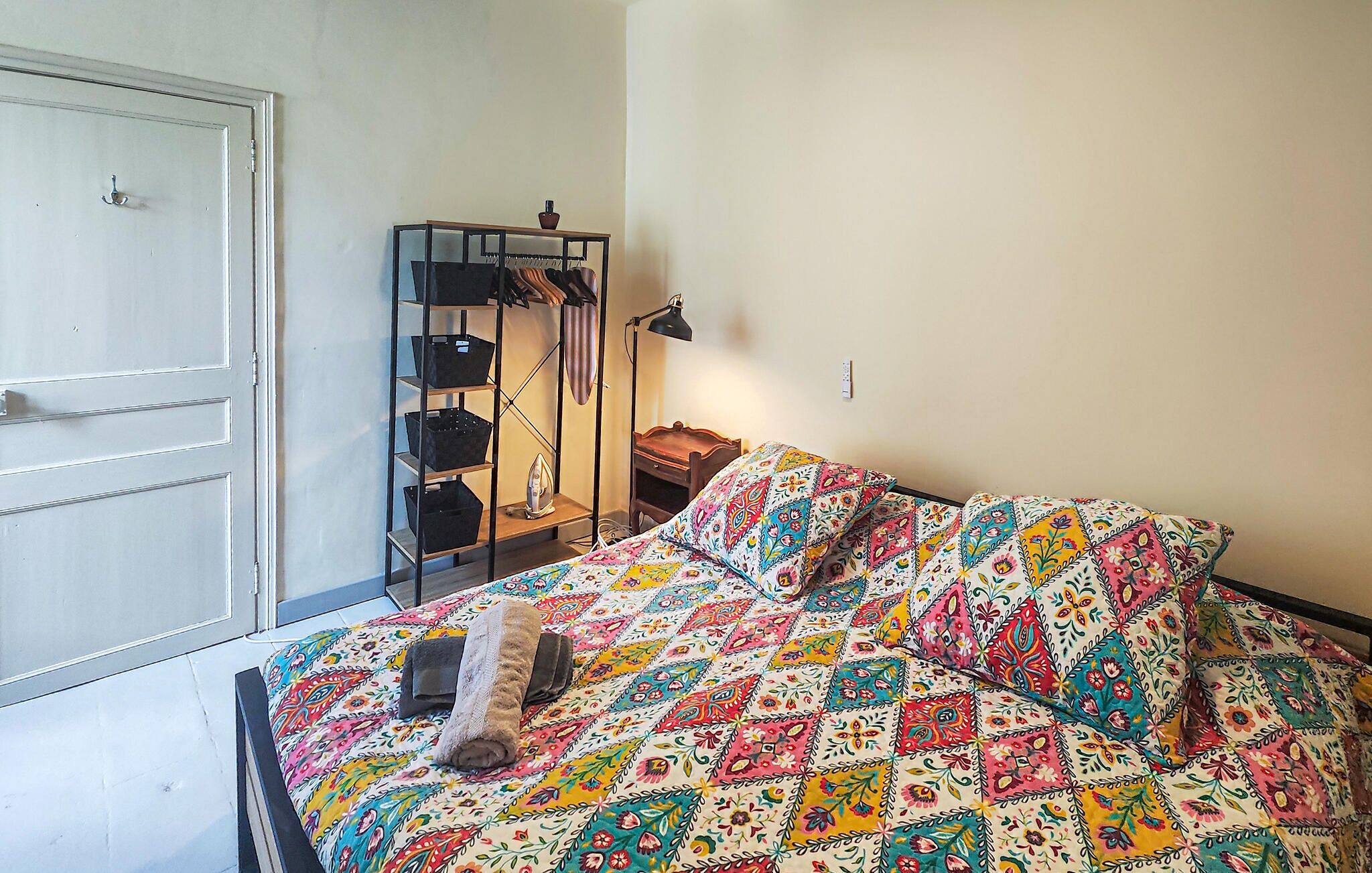 Een slaapkamer met een bed, een kast, een plank met opbergmanden en een lamp.