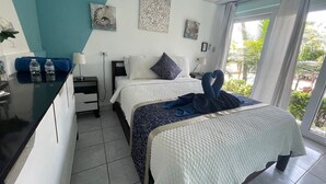 A hotel room with a bed, bedside tables, a desk, and a view of the outdoors. - Rancho Matnik a Hidden Paradise (La Paz)