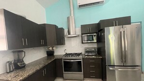 A compact kitchen with dark cabinets, a gas stove, a microwave, a toaster, and a stainless steel refrigerator. - Rancho Matnik a Hidden Paradise (La Paz)