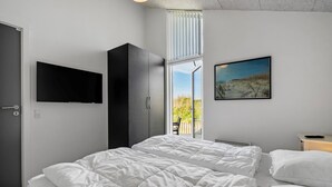 Un dormitorio con cama, televisión, ventana con persianas y un cuadro en la pared.