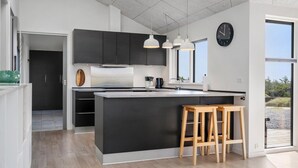 Una cocina moderna con una isla grande, luces colgantes y un reloj en la pared.