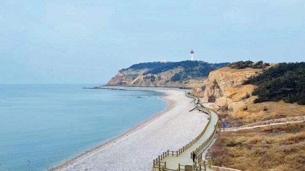 Un paysage côtier avec une plage, un phare et une falaise rocheuse.